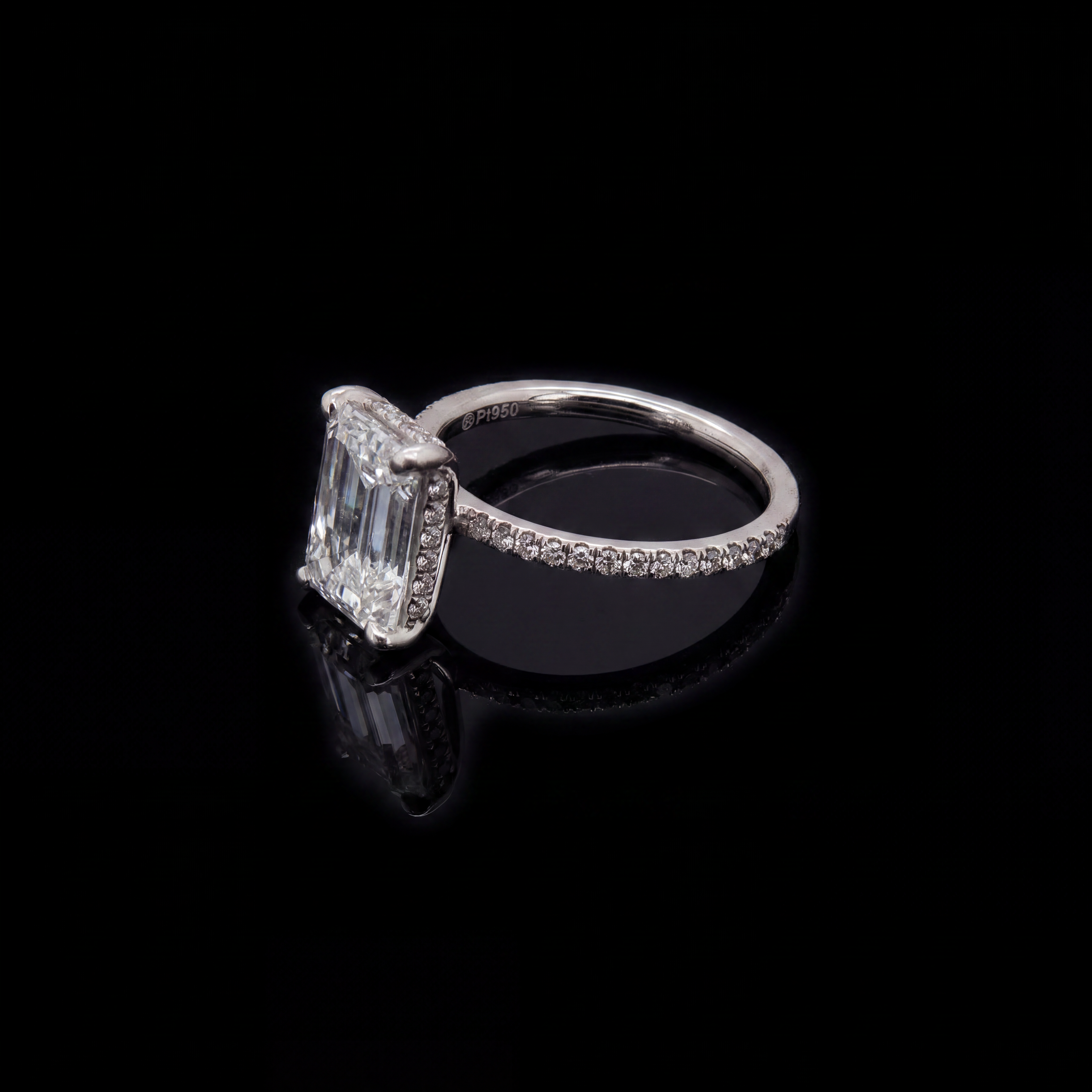 Side view of a ring with an elongated clear centre stone on a black reflective background