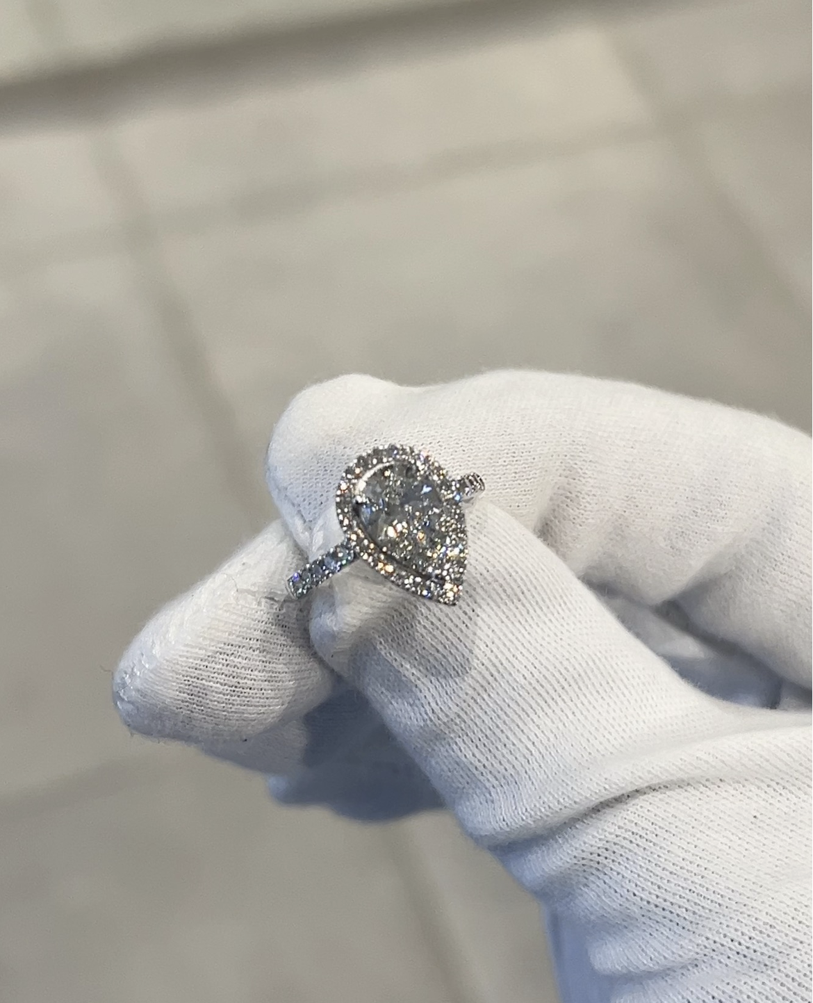Pear-shaped ring with a clear centre stone and surrounding clear stones held in a white-gloved hand