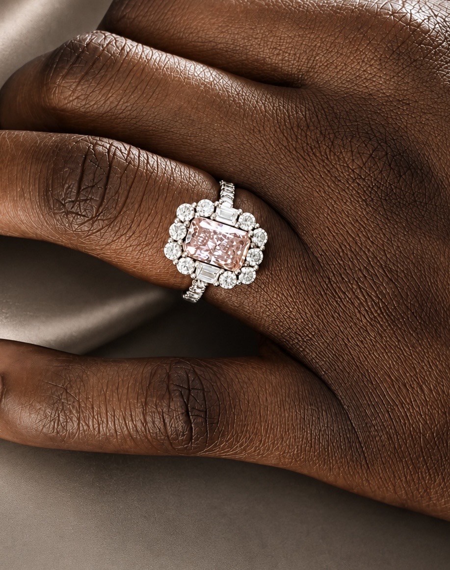 Ring with a rectangular pale-pink centre stone and surrounding clear stones, worn on a hand